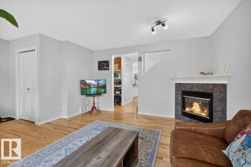 Living area featuring wood-finish flooring, a tiled fireplace with a mantel, track lighting, and a white paneled door - 722 88A Street Sw, Edmonton, AB - Indoor Photo Showing Living Room With Fireplace