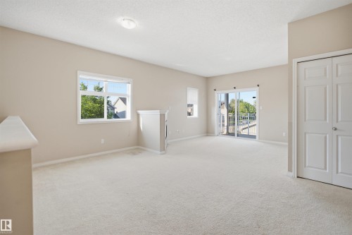 Spacious room featuring light-colored carpeting, a large picture window, a built-in architectural feature, a sliding glass door to an exterior space, and a double-door closet - #95 3040 Spence Wd Sw, Edmonton, AB - Indoor Photo Showing Other Room