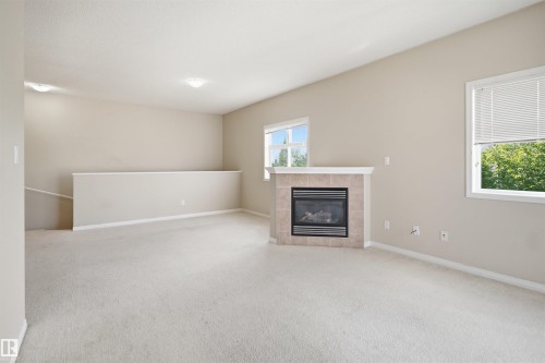 Spacious great room with neutral carpet flooring, gas fireplace with stone surround, recessed ceiling lighting, and abundant natural light from multiple windows - #95 3040 Spence Wd Sw, Edmonton, AB - Indoor With Fireplace