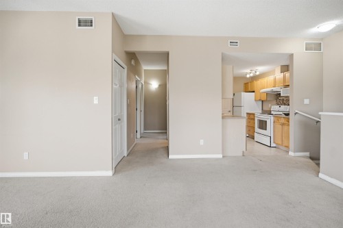 Open concept living space featuring neutral carpet flooring and a kitchen with light wood cabinetry, white appliances, and a tiled backsplash - #95 3040 Spence Wd Sw, Edmonton, AB - Indoor