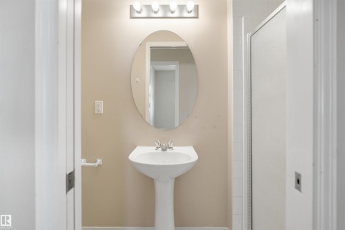 Pedestal sink with chrome faucet, an oval mirror, and a vanity light fixture featuring four bulbs - #95 3040 Spence Wd Sw, Edmonton, AB - Indoor Photo Showing Bathroom