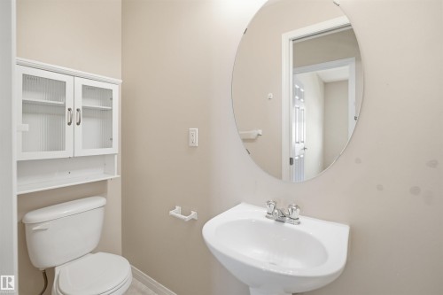 Pedestal sink with a chrome faucet, oval mirror, and an over-toilet storage cabinet with fluted glass doors - #95 3040 Spence Wd Sw, Edmonton, AB - Indoor Photo Showing Bathroom