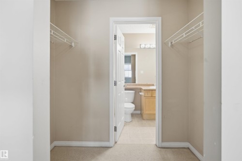 Walk-through closet with wire shelving leading to a bathroom featuring a light wood vanity, a neutral countertop, and a four-bulb light fixture - #95 3040 Spence Wd Sw, Edmonton, AB - Indoor Photo Showing Bathroom