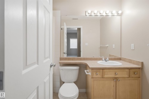 Bathroom vanity featuring an integrated sink, laminate countertop, light wood-finish cabinetry, and a large wall-mounted mirror with overhead bar lighting - #95 3040 Spence Wd Sw, Edmonton, AB - Indoor Photo Showing Bathroom