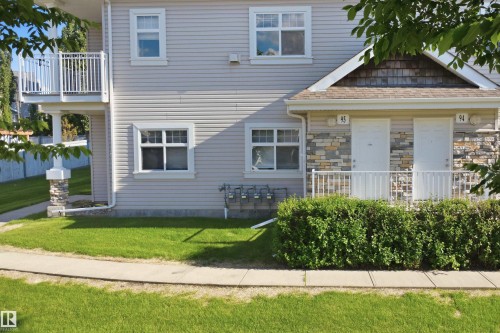 Two-story exterior featuring light-colored siding, a stone facade accent, and multiple windows with white trim - #95 3040 Spence Wd Sw, Edmonton, AB - Outdoor