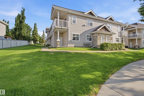 Contemporary multi-level residence featuring light-toned siding, stone accents, multiple balconies with white railings, a paved sidewalk, and expansive green lawn areas - #95 3040 Spence Wd Sw, Edmonton, AB - Outdoor