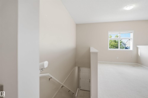 Carpeted loft area featuring a double-paned window, neutral wall paint, overhead lighting, and a white interior door at the base of the stairs - #95 3040 Spence Wd Sw, Edmonton, AB - Indoor Photo Showing Other Room