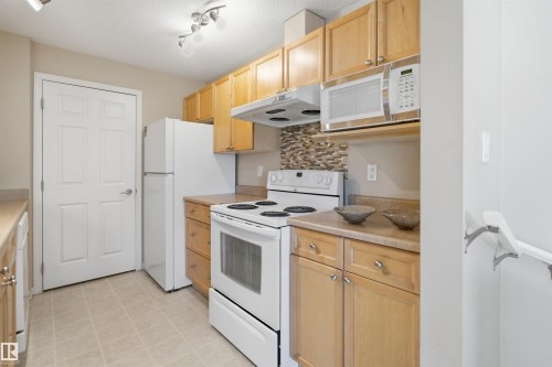 Kitchen featuring light wood cabinetry, white appliances, a patterned tile backsplash, and light-toned countertops - #95 3040 Spence Wd Sw, Edmonton, AB - Indoor Photo Showing Kitchen