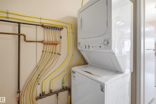 Utility area featuring a stacked white washer and dryer unit, extensive PEX plumbing, and visible copper and yellow gas lines - #95 3040 Spence Wd Sw, Edmonton, AB - Indoor Photo Showing Laundry Room
