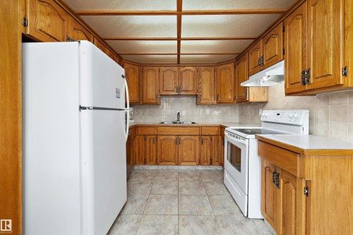Galley kitchen featuring wood-finish cabinetry throughout, ceramic tile flooring, white appliances including refrigerator and electric range, and overhead lighting - 3511 73 Street Nw, Edmonton, AB 