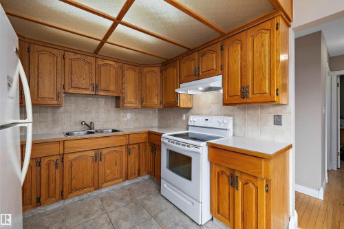Wood-finish cabinetry with dark hardware, solid surface countertops, a tile backsplash, and a drop ceiling with integrated lighting - 3511 73 Street Nw, Edmonton, AB 
