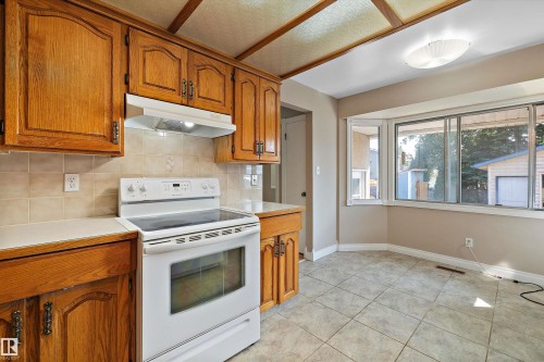 Kitchen featuring wood cabinetry, a tile backsplash, a built-in range, and a tiled floor - 3511 73 Street Nw, Edmonton, AB 