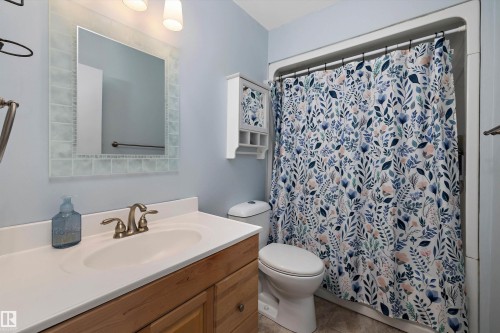 Spa-inspired bathroom featuring a wood-finish vanity with dual-sink white countertop, brushed bronze faucet, and ample storage - 3511 73 Street Nw, Edmonton, AB 