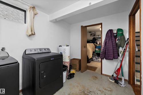 Utility room featuring side-by-side laundry appliances, concrete flooring, wood-frame doorway with access to adjacent storage closet, and white painted walls with exposed ceiling beams - 3511 73 Street Nw, Edmonton, AB 