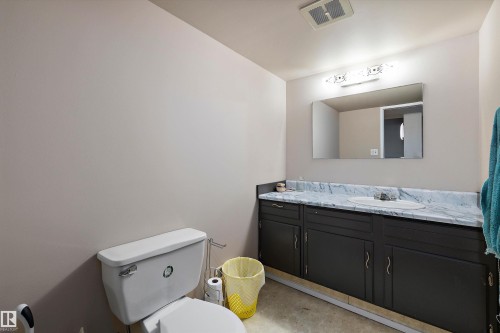 Spacious bathroom vanity with an integrated sink, broad wall mirror, vanity lighting, and a white toilet - 3511 73 Street Nw, Edmonton, AB 
