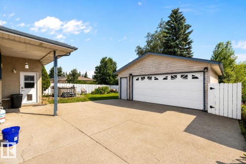 Detached garage with a paneled door, expansive concrete driveway, and a white picket fence - 3511 73 Street Nw, Edmonton, AB 