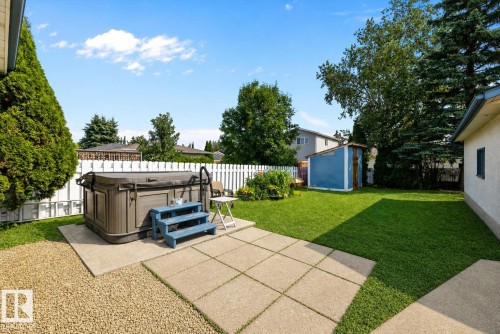 Spacious backyard featuring a hot tub on a concrete pad, a white picket fence, an expansive lawn, and a storage shed - 3511 73 Street Nw, Edmonton, AB 