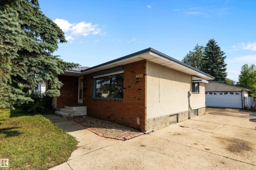 Brick ranch-style home featuring a modern pitched roof, expansive driveway with attached garage, mature landscaping with established trees and shrubs, front entry with large window, and level lot with manicured lawn - 3511 73 Street Nw, Edmonton, AB 