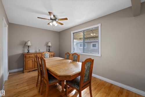 Elegant dining room showcasing warm wood-finish flooring, a ceiling fan with integrated lighting, and large windows providing natural illumination - 3511 73 Street Nw, Edmonton, AB 