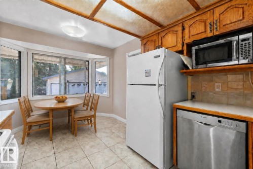 Kitchen featuring wood cabinetry, a bay window, tile flooring, and integrated stainless steel appliances - 3511 73 Street Nw, Edmonton, AB 