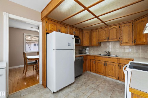 Spacious kitchen featuring warm wood cabinetry, tile countertops, and stainless steel appliances including a white refrigerator and electric range - 3511 73 Street Nw, Edmonton, AB 