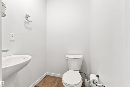 Powder room featuring a pedestal sink, white toilet, wood-finish flooring, and white walls - 1172 Aster Boulevard Nw Nw, Edmonton, AB - Indoor Photo Showing Bathroom