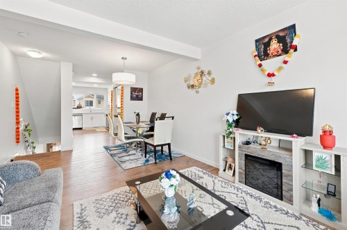 Open-concept living space featuring wood-finish flooring, a contemporary fireplace unit with integrated shelving, and a dining area with a modern pendant light fixture - 1172 Aster Boulevard Nw Nw, Edmonton, AB - Indoor Photo Showing Living Room With Fireplace