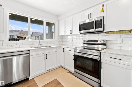 Bright kitchen featuring white shaker cabinetry, stainless steel appliances, white subway tile backsplash, light countertops, and wood-finish flooring - 1172 Aster Boulevard Nw Nw, Edmonton, AB - Indoor Photo Showing Kitchen With Stainless Steel Kitchen With Double Sink