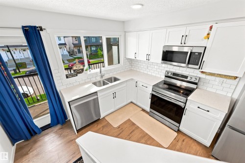 Modern kitchen featuring white shaker cabinetry, stainless steel appliances, light-toned countertops, and a subway tile backsplash - 1172 Aster Boulevard Nw Nw, Edmonton, AB - Indoor Photo Showing Kitchen With Stainless Steel Kitchen With Double Sink