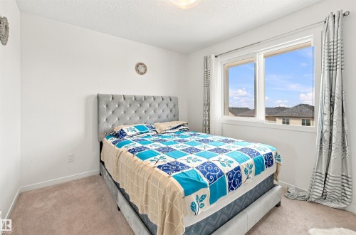 Bright secondary bedroom featuring a tufted upholstered headboard, carpeted flooring, and large picture windows framing mountain vistas - 1172 Aster Boulevard Nw Nw, Edmonton, AB - Indoor Photo Showing Bedroom