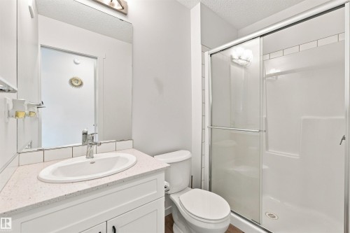 Bathroom featuring a white vanity with an undermount sink, a light-colored speckled countertop, a large frameless mirror, and a shower with a sliding glass door - 1172 Aster Boulevard Nw Nw, Edmonton, AB - Indoor Photo Showing Bathroom