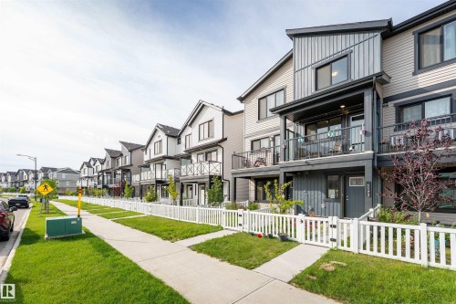 Modern townhome featuring a balcony, contemporary siding, white picket fencing, an attached front porch, and mature landscaping - 1172 Aster Boulevard Nw Nw, Edmonton, AB - Outdoor With Balcony