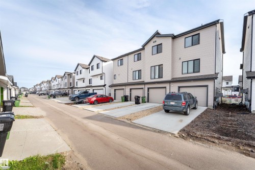 Modern townhouse exterior featuring light-colored siding, dark trim, a gabled roofline, and an integrated garage - 1172 Aster Boulevard Nw Nw, Edmonton, AB - Outdoor With Facade