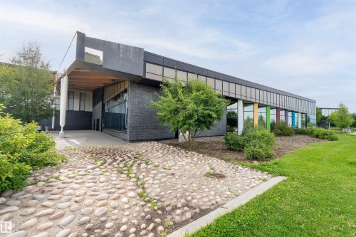 Modern commercial building featuring extensive glass curtain walls, a distinctive pebbled entryway, and a lush green lawn - 1172 Aster Boulevard Nw Nw, Edmonton, AB - Outdoor