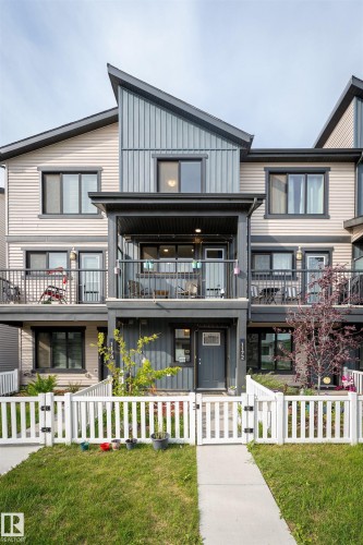 Modern townhouse exterior featuring a white picket fence, a concrete walkway, a covered entry, and an upper-level balcony - 1172 Aster Boulevard Nw Nw, Edmonton, AB - Outdoor With Balcony With Facade