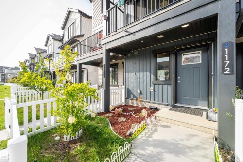 Modern townhouse exterior featuring a gray entrance door, vertical siding, and a covered porch - 1172 Aster Boulevard Nw Nw, Edmonton, AB - Outdoor