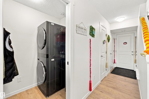 Dedicated laundry area featuring a stacked front-load washer and dryer unit, wood-finish flooring, and crisp white walls - 1172 Aster Boulevard Nw Nw, Edmonton, AB - Indoor Photo Showing Laundry Room