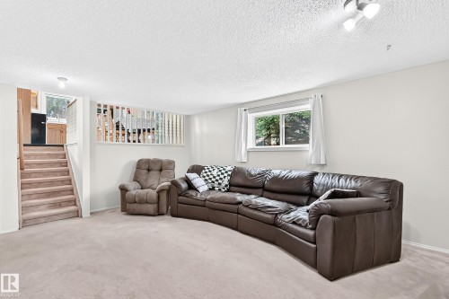 Carpeted flooring extending to the staircase, white painted walls, natural light from a double window, and a built-in privacy screen - 2404 37 Street Nw, Edmonton, AB - Indoor Photo Showing Living Room