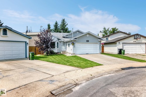 Light gray siding exterior with a white garage door, concrete driveway, and a manicured front lawn - 2404 37 Street Nw, Edmonton, AB - Outdoor