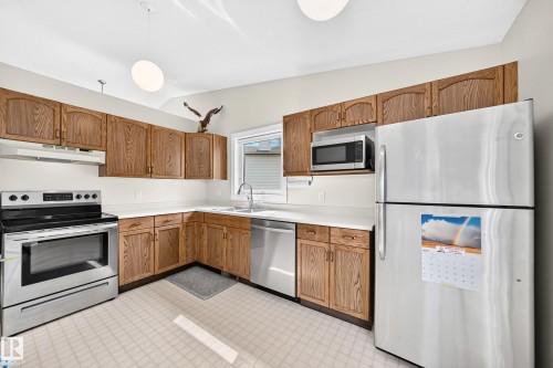 Kitchen featuring wood-finish cabinetry, stainless steel appliances, and a double basin sink - 2404 37 Street Nw, Edmonton, AB - Indoor Photo Showing Kitchen With Double Sink