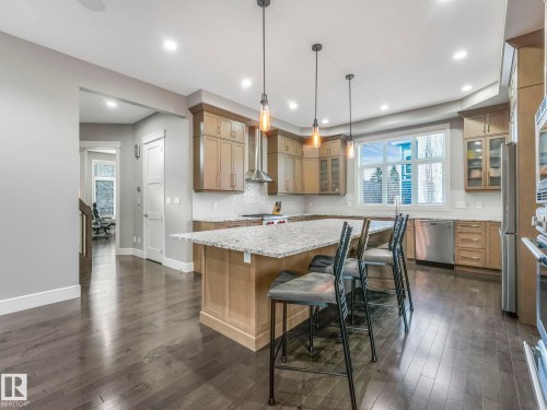 Spacious kitchen featuring a large island with seating, stainless steel appliances, wood-finish flooring, and pendant lighting - 8927 120 Street Nw, Edmonton, AB - Indoor
