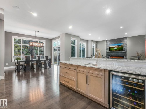 Open-concept interior featuring wood-finish flooring, a stone-clad fireplace, and a built-in wine cooler - 8927 120 Street Nw, Edmonton, AB - Indoor