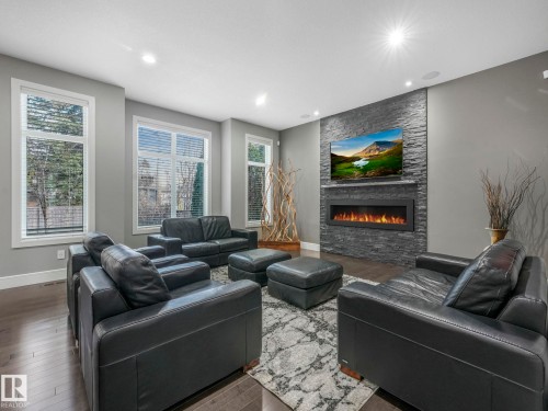 Expansive living space featuring wood-finish flooring, multiple windows, recessed ceiling lighting, and a stone-clad fireplace with an integrated electronic firebox - 8927 120 Street Nw, Edmonton, AB - Indoor Photo Showing Living Room With Fireplace