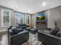 Expansive living space featuring wood-finish flooring, multiple windows, recessed ceiling lighting, and a stone-clad fireplace with an integrated electronic firebox - 