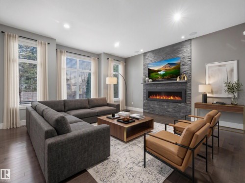 Virtually staged - Spacious living area featuring dark wood-finish flooring, a contemporary fireplace with a stacked stone facade, and recessed ceiling lighting - 8927 120 Street Nw, Edmonton, AB - Indoor Photo Showing Living Room With Fireplace