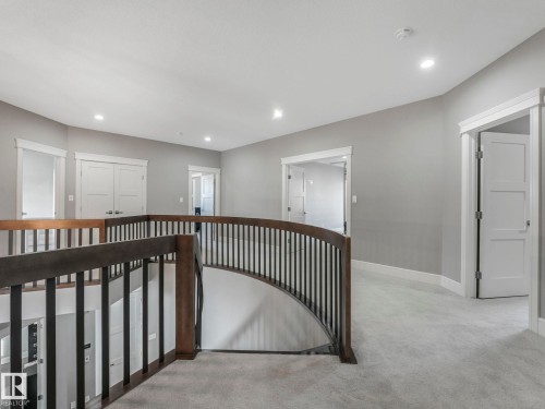 Curved staircase with wood-finish handrail and black balusters - 8927 120 Street Nw, Edmonton, AB - Indoor Photo Showing Other Room