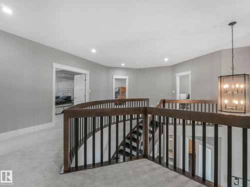 Carpeted upper-level landing with wrought iron and wood-finish railing, recessed lighting, and a suspended chandelier - 8927 120 Street Nw, Edmonton, AB - Indoor Photo Showing Other Room