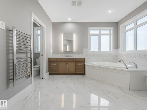 Polished tile flooring, built-in soaking tub with paneling, wood-finish vanity with dual sinks, wall-mounted mirror with integrated lighting, and multiple window installations - 8927 120 Street Nw, Edmonton, AB - Indoor Photo Showing Bathroom