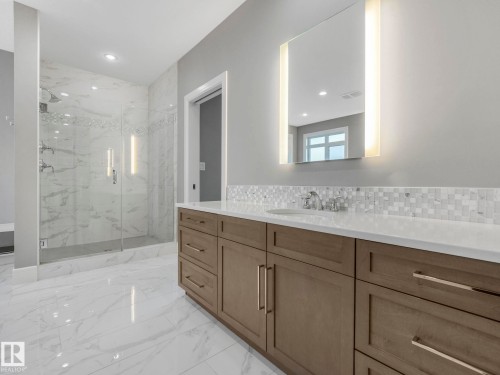 Large format tile flooring, extensive wood-finish cabinetry, quartz countertop, glass-enclosed shower with tile surround, and illuminated vanity mirror - 8927 120 Street Nw, Edmonton, AB - Indoor Photo Showing Bathroom