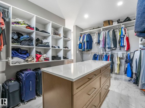 Central island with light-toned countertop, built-in shelving, multiple hanging rods, recessed lighting, and tile flooring - 8927 120 Street Nw, Edmonton, AB - Indoor With Storage